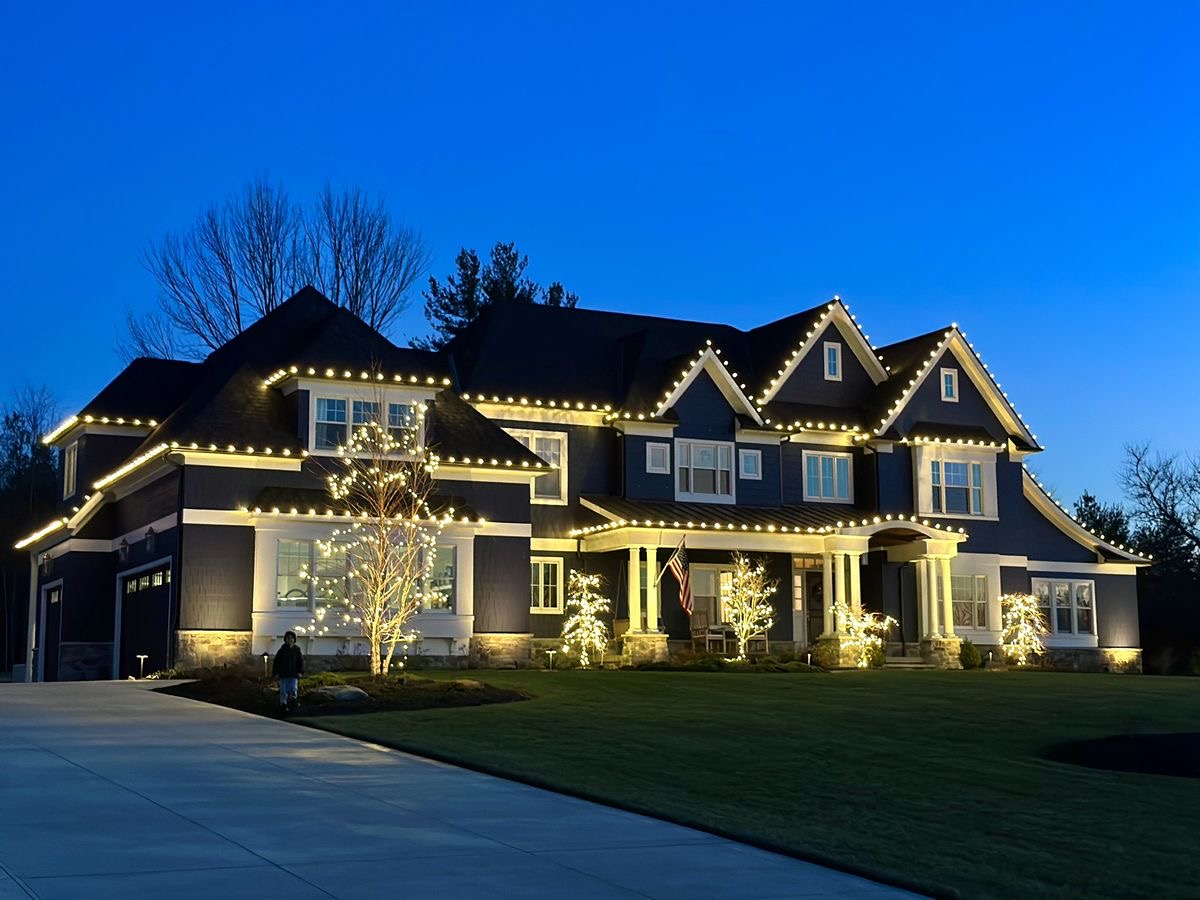 Navy two-story estate with roofline lights and lit trees along the front
