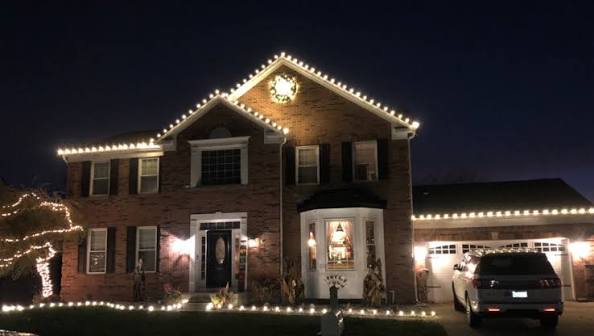 Two-story brick home with warm white roofline lights and lit wreath