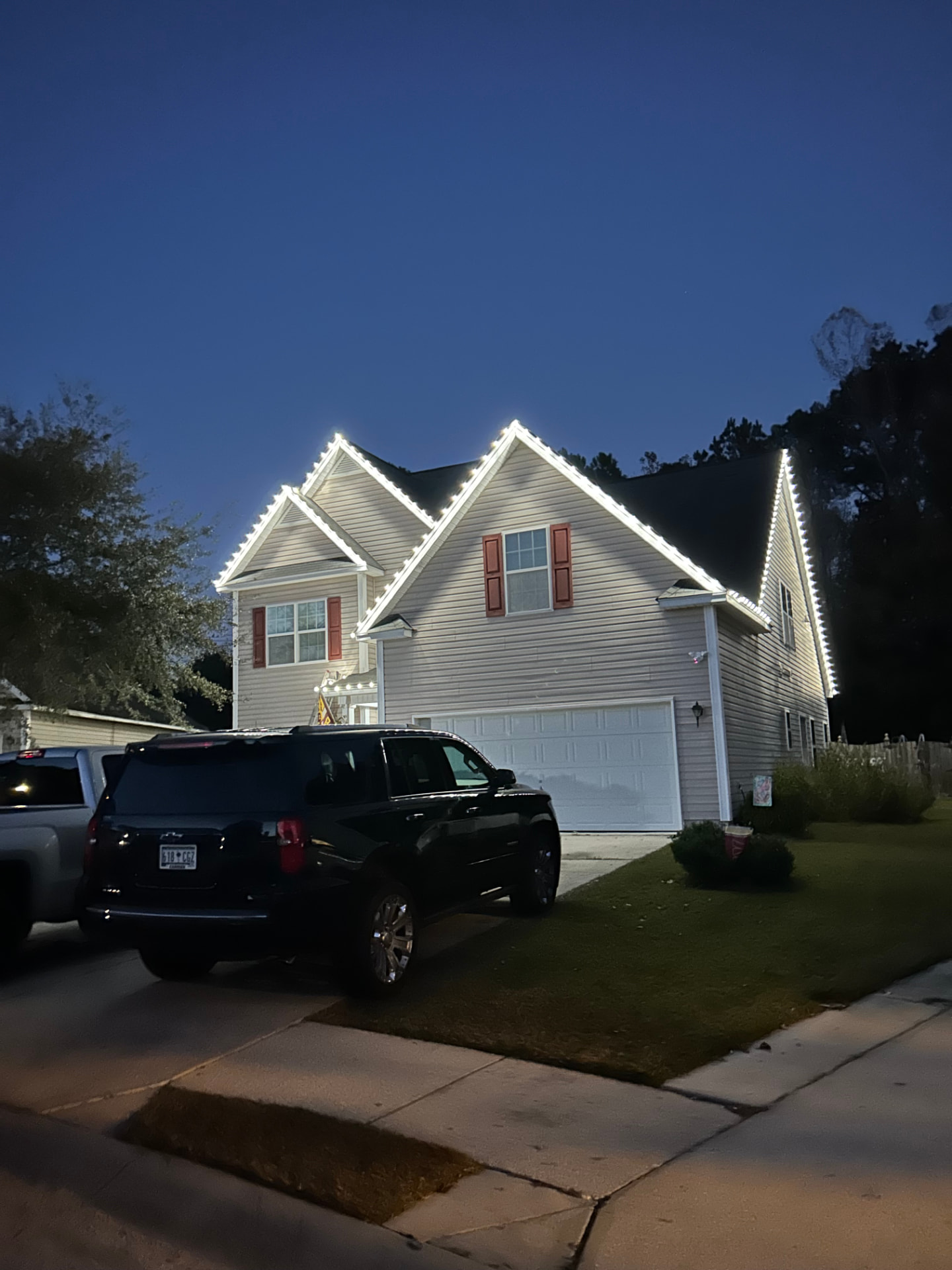 Two-story home with white lights tracing the gables and garage at night
