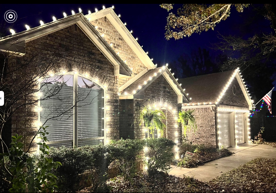 Brick home with lights around arched windows, ferns, and garage