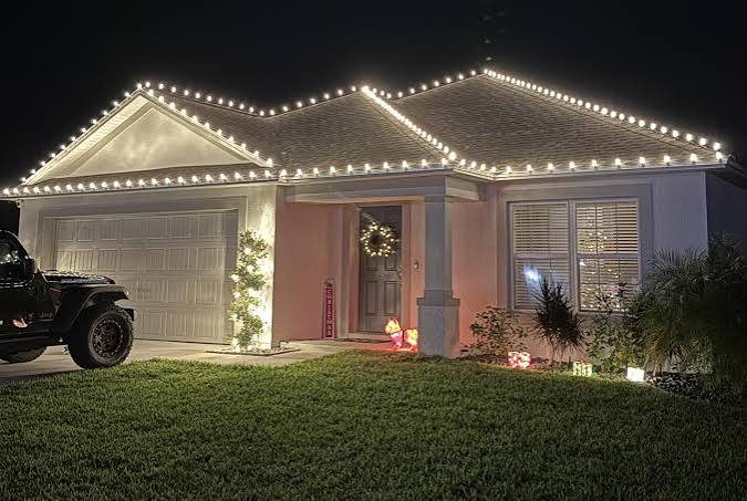 Single-story home with roofline lights, lit wreath, and holiday decor